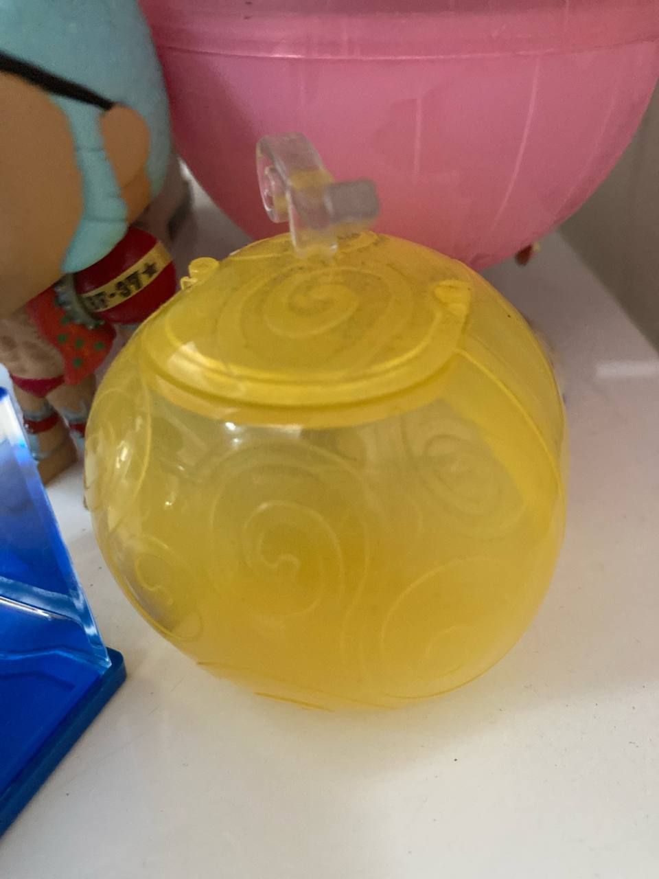 Capsule One Piece jaune translucide, fermée, sur une étagère blanche