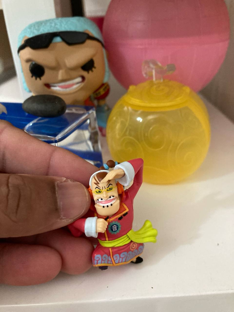 Figurine One Piece en main, boule jaune et Funko Franky en arrière-plan